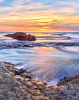 Ocean water flowing over rock reef at sunset with soft golden light