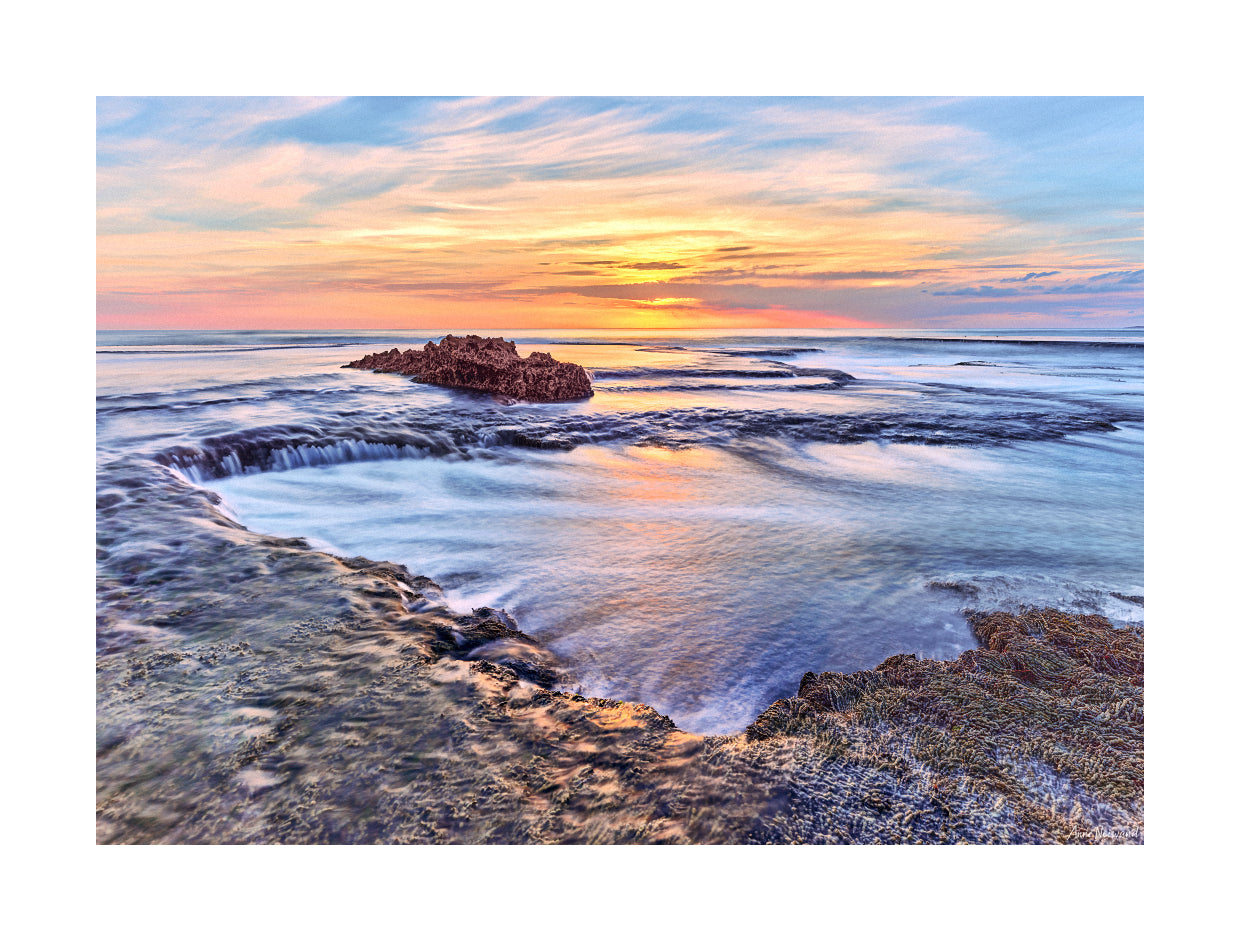 Ocean retreating gently across reef under soft light and wide sky